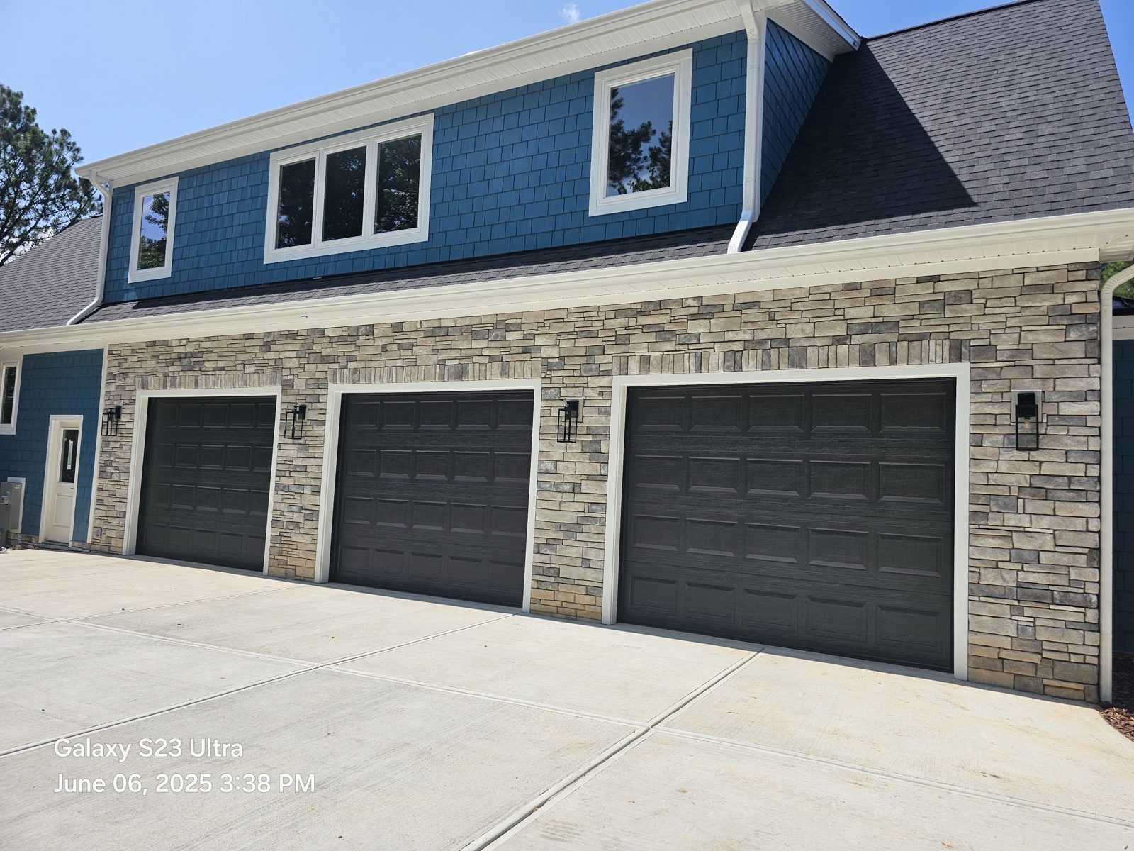 Three gray garage doors installed on a blue home by Premier Access Solutions