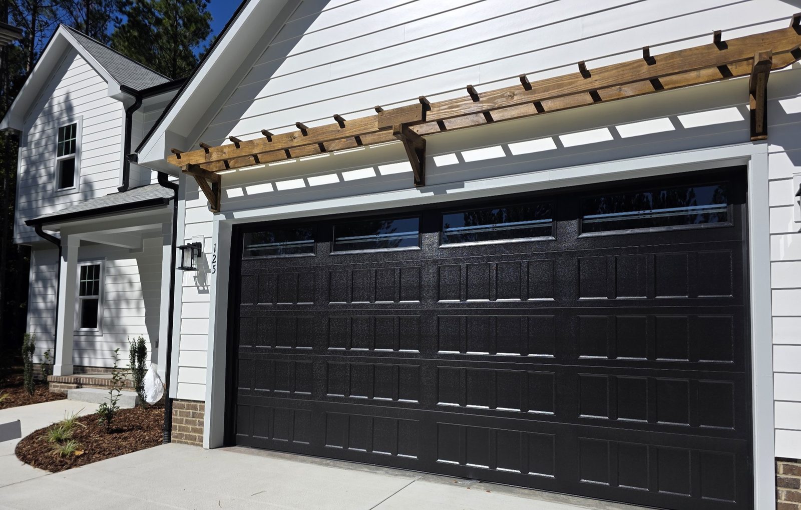 Black raised-panel garage door with windows installed on a white home by Premier Access Solutions